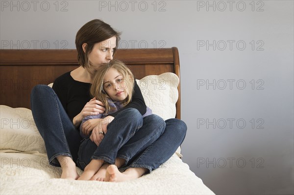 Caucasian mother cuddling daughter on sofa