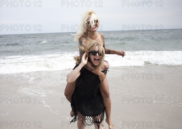 Woman carrying friend piggyback on beach