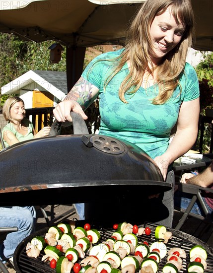 Smiling woman grilling kebabs in backyard