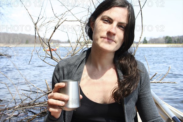 Woman drinking with metal cup in boat on lake