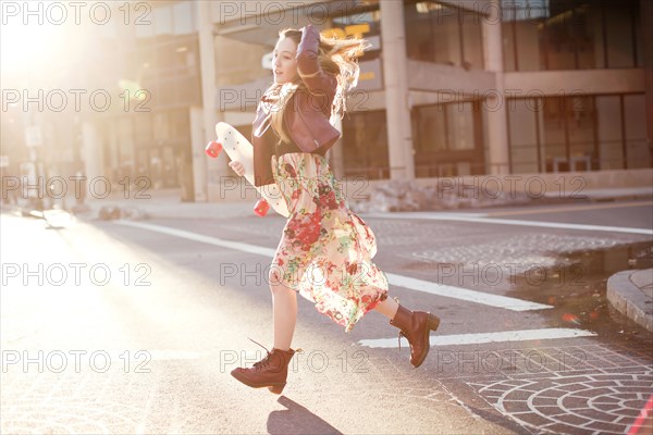 Woman carrying skateboard in city intersection