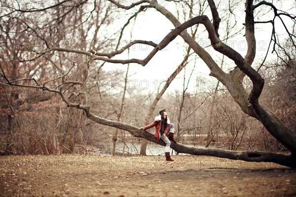 Caucasian woman sitting in tree in rural field