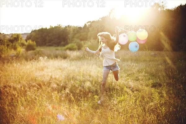 Girl running with balloons in sunny field