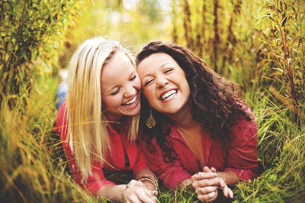 Laughing women laying together in tall grass