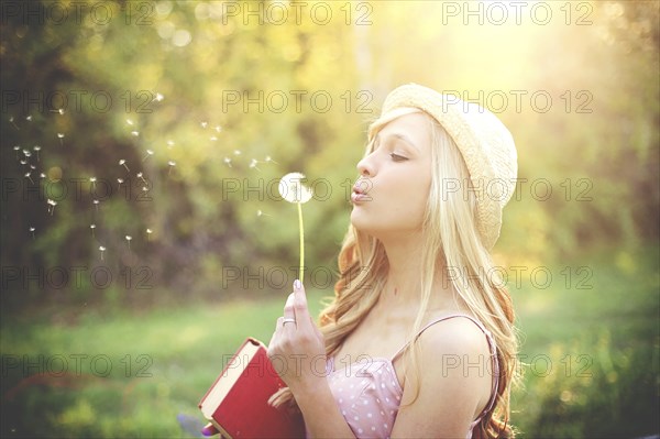 Woman blowing dandelion seeds in rural field
