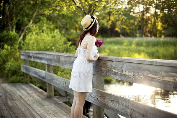 Caucasian woman standing on bridge over rural pond