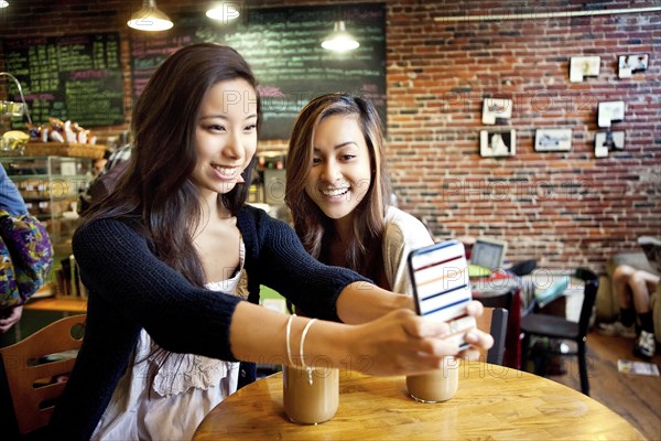 Women taking selfie with cell phone at cafe table