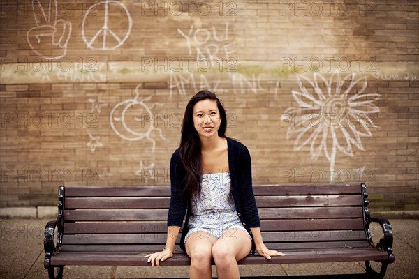 Woman sitting on urban bench near graffiti wall