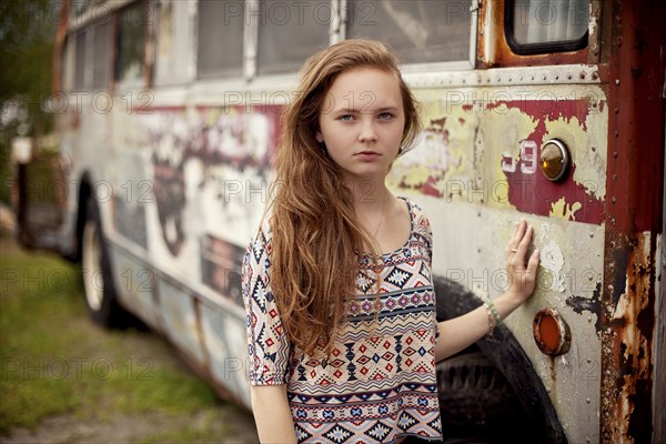 Caucasian teenage girl standing near dilapidated bus