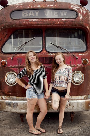 Smiling girls holding hands near dilapidated bus