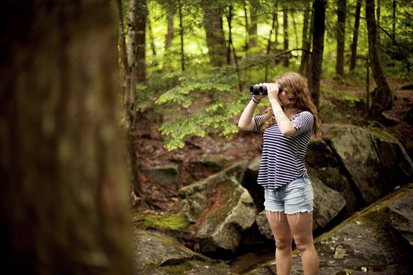 Girl looking through binoculars in forest