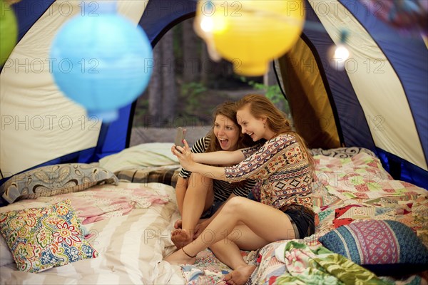 Girls taking selfie with cell phone in camping tent