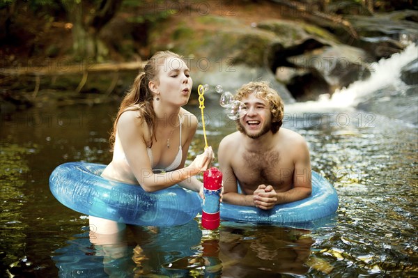 Couple blowing bubbles in forest river