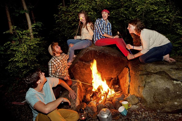 Friends roasting marshmallows over forest campfire