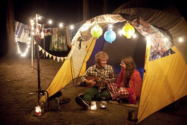Couple playing music in camping tent at night