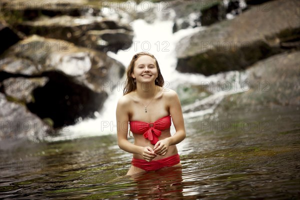 Caucasian teenage girl standing in river near waterfall