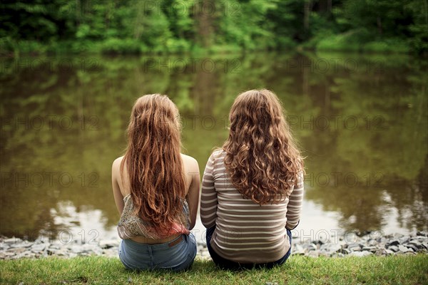 Rear view of girls sitting near lake