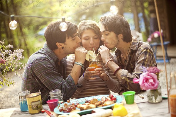 Friends sharing soda at picnic table in forest