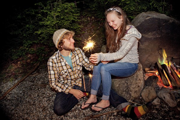 Couple playing with sparkler near campfire