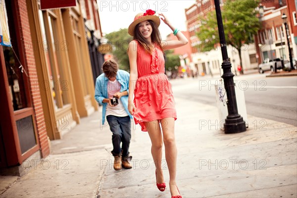 Boy photographing girlfriend on city sidewalk