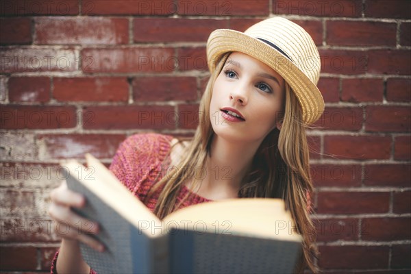 Girl reading book near brick wall