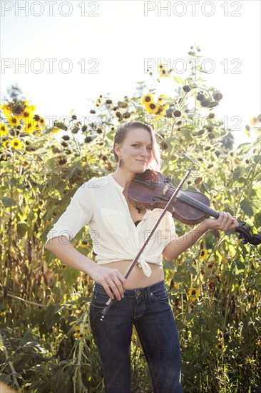 Caucasian musician playing violin in sunflower garden