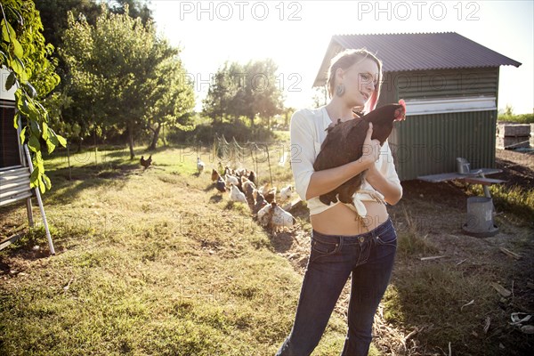 Caucasian farmer holding chicken by hen house