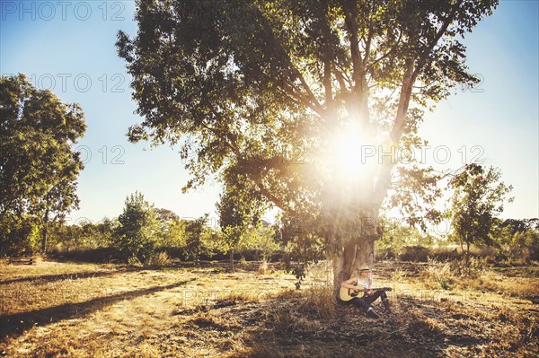 Caucasian musician playing guitar in rural field