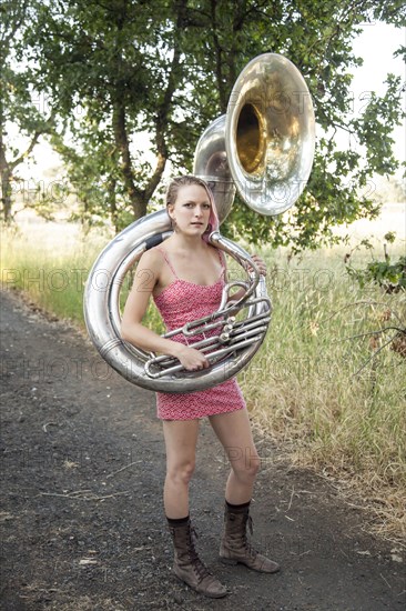 Caucasian musician carrying tuba on dirt path