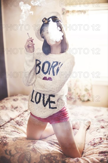 Caucasian girl in captain hat smoking cigarette on bed