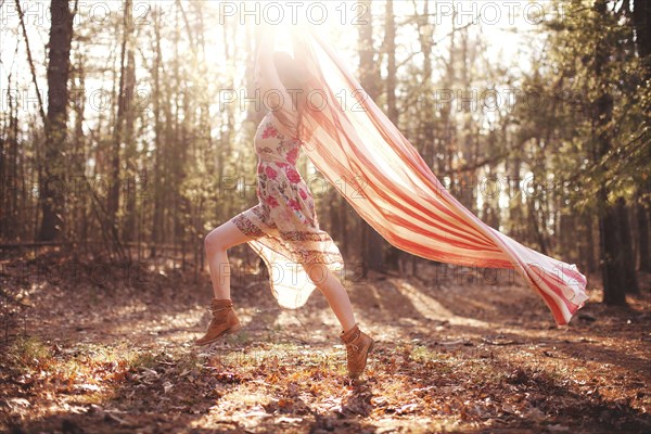 Hispanic woman running with scarf in forest