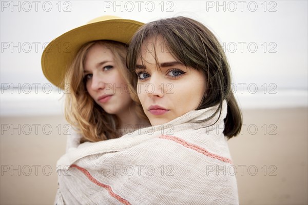 Caucasian friends wrapped in blanket on beach