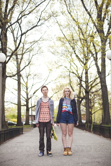 Caucasian couple standing in park with skateboard