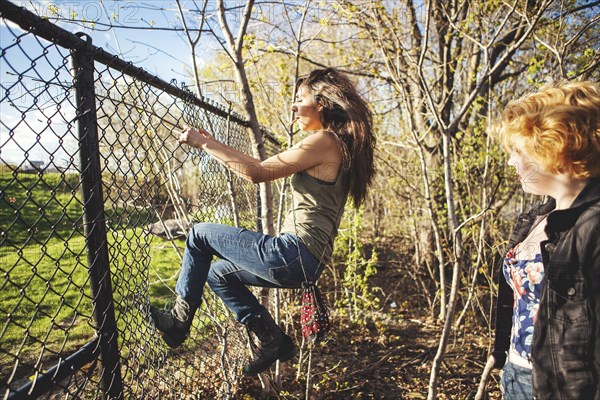 Women climbing through hole in chain-link fence