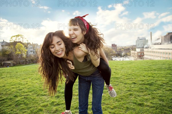 Woman carrying friend piggyback in urban park