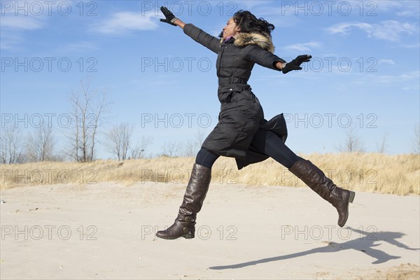 Woman in coat jumping for joy on beach