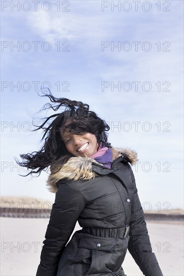 Woman in coat jumping for joy on beach