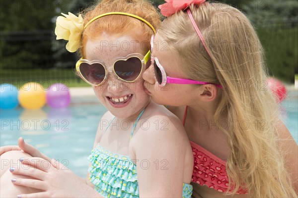 Caucasian girl kissing cheek of friend near swimming pool