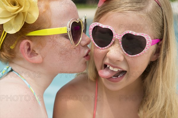 Caucasian girl kissing cheek of friend near swimming pool