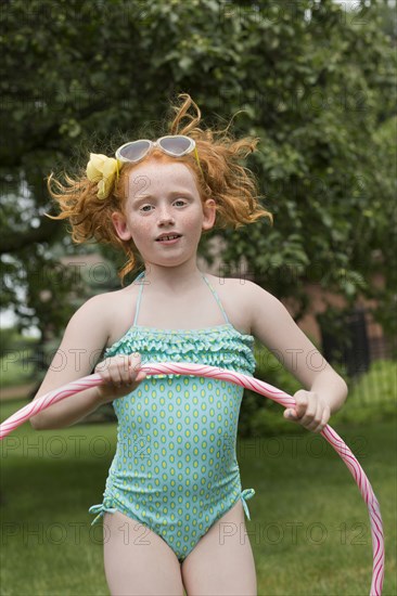 Caucasian girl jumping with plastic hoop in field