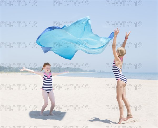 Caucasian girls playing with fabric on beach