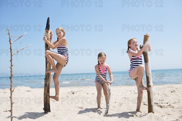 Caucasian girls climbing poles on beach