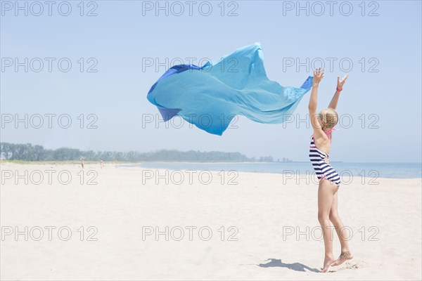 Caucasian girl playing with fabric on beach