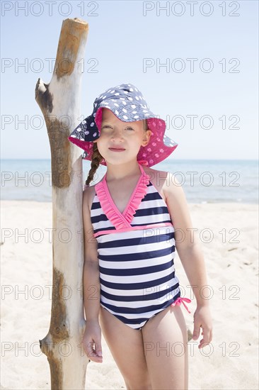 Caucasian girl leaning on wooden pole on beach