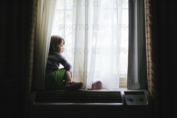 Mixed race girl sitting in window