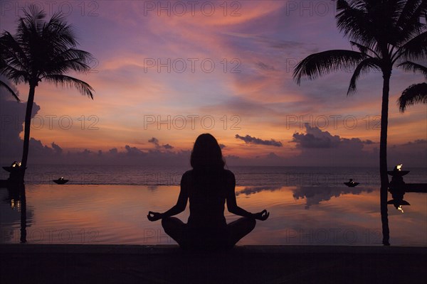 Silhouette of woman meditating near swimming pool at sunset