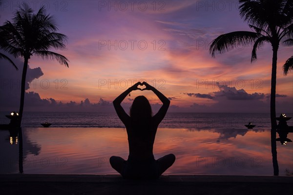 Silhouette of woman gesturing love near swimming pool at sunset