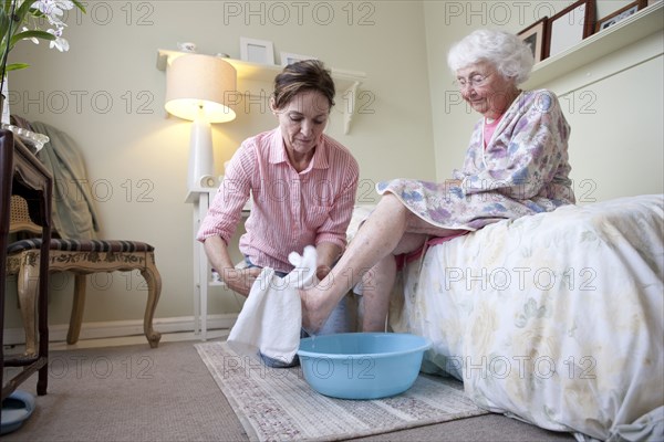 Caregiver washing foot of older woman in bedroom