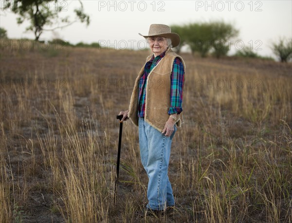 Older Caucasian woman walking with cane in field