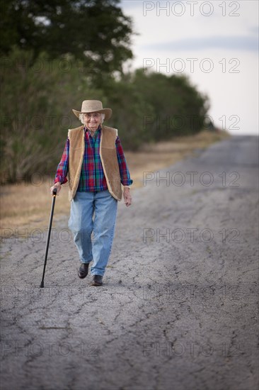 Older Caucasian woman walking with cane on rural road